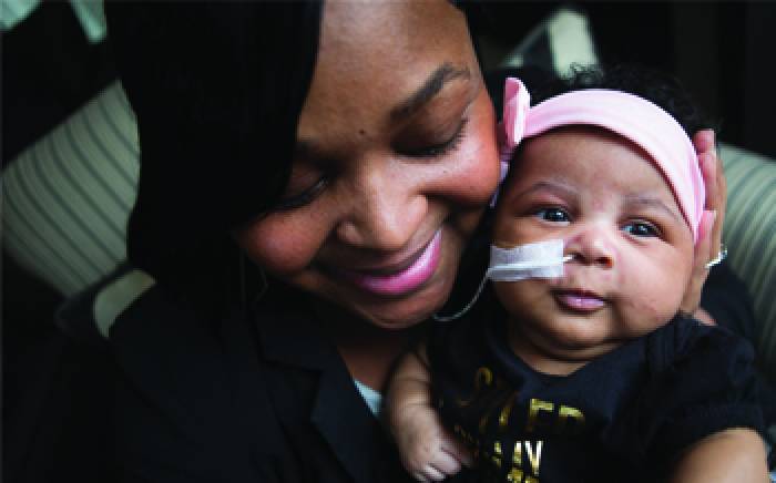 Mom holding a small baby near her face, with a pink headband and a feeding tube
