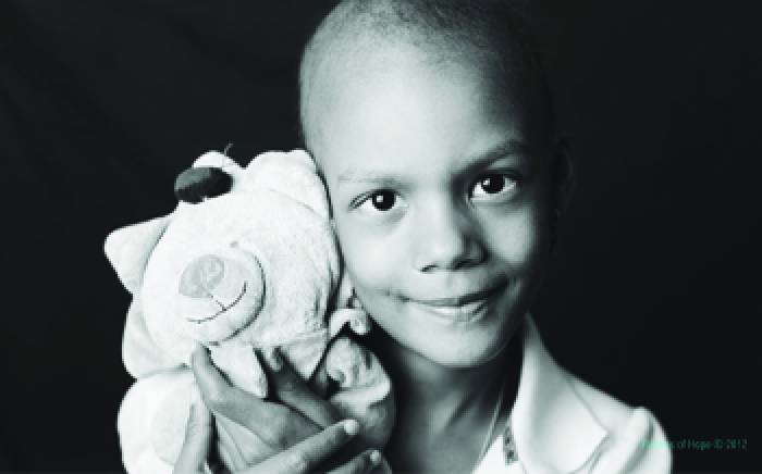 A young girl. She is bald and holding a teddy bear.