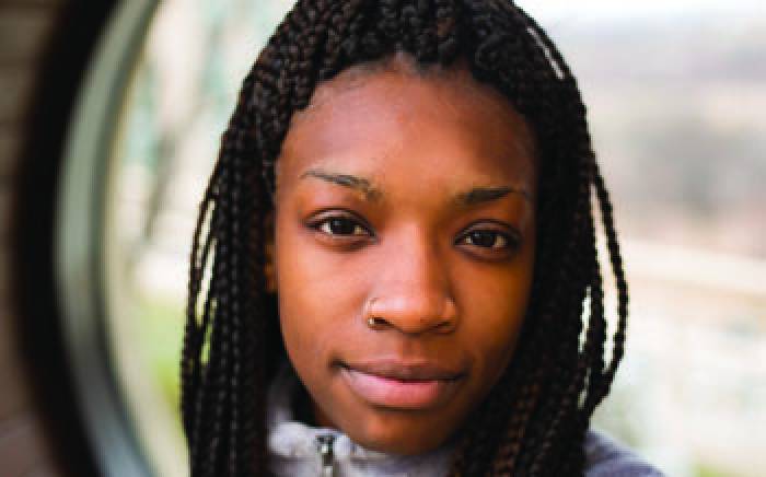 A close up shot of a young woman, she has long braids and a scar on her right eyebrow.