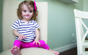 A small girl sitting on a chair with a pink bow in her hair.