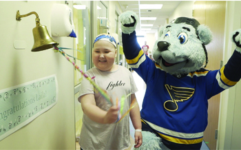 A young girl ringing a bell next to the St. Louis Blues' hockey mascot, a polar bear in a blue jersey. 