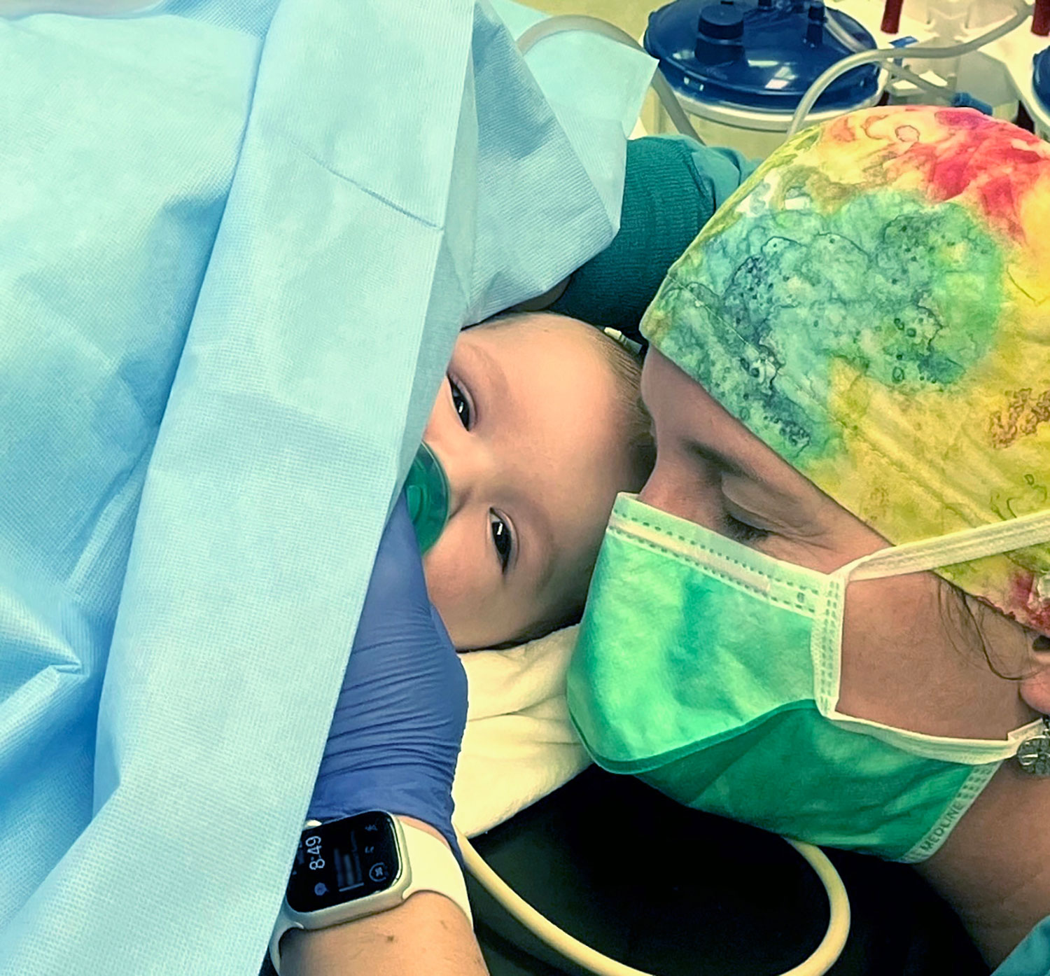 Baby lying down next to a woman with a face mask