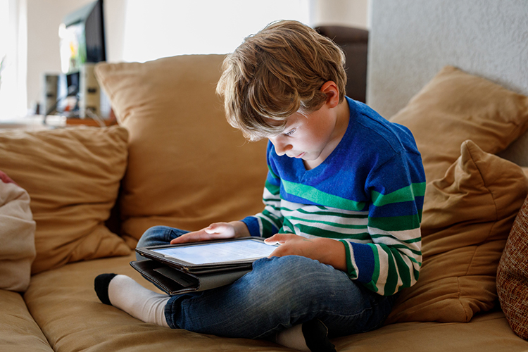 Young boy looking at a tablet while sitting on a couch