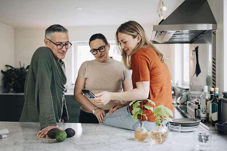 Mom, dad, and daughter looking at the daughter's phone in the kitchen