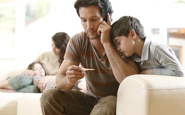 Dad looking at a thermometer while sitting with his son next to him