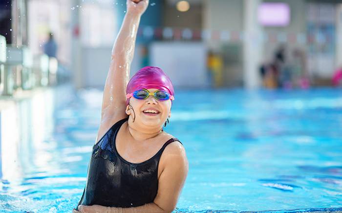 Girl swimmer holding her hand up high while standing in a pool