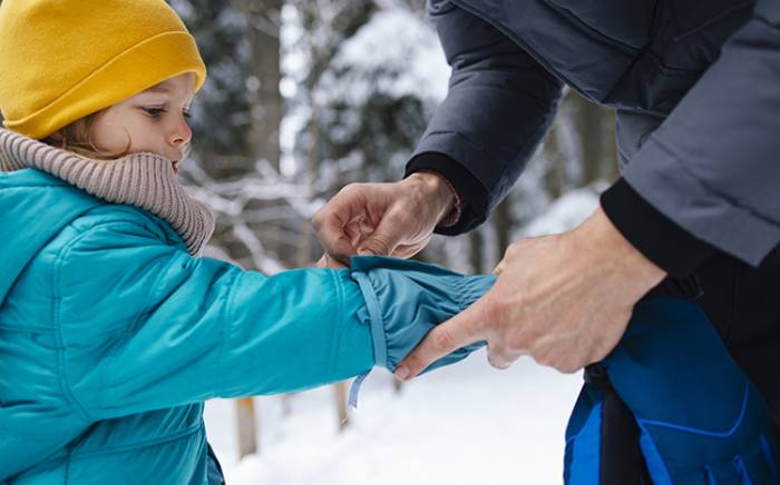 Parent helping fit/adjust the jacket sleeve of a child