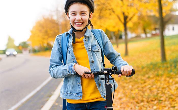 Young girl riding a scooter with a helmet on