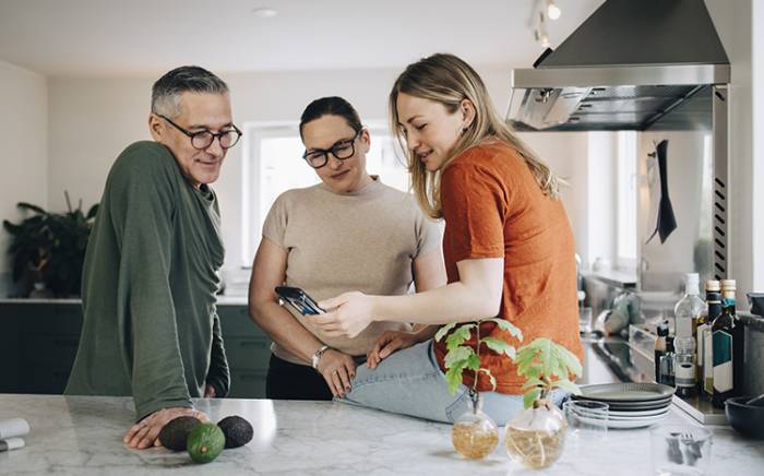 Mom, dad, and daughter looking at the daughter's phone in the kitchen